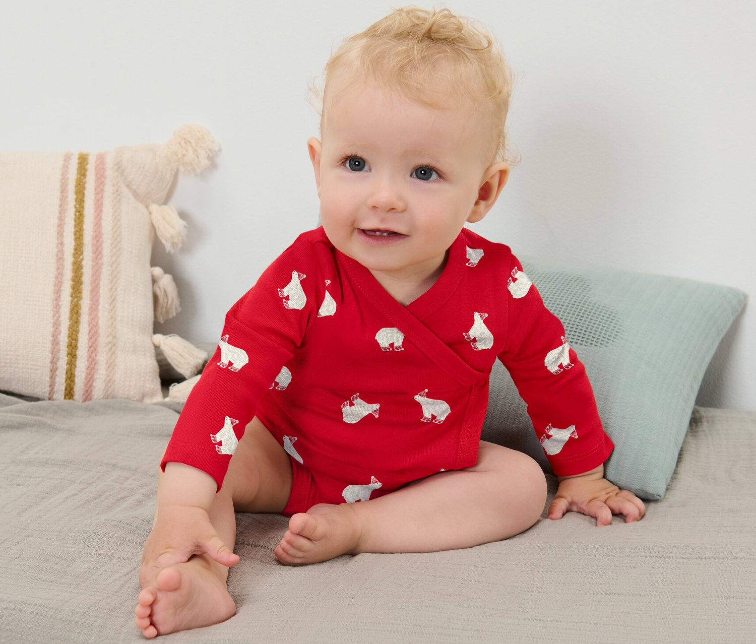 Kojenecké dívky v červeném body s dlouhým rukávem s potiskem ledních medvědů sedí na šedé dece.