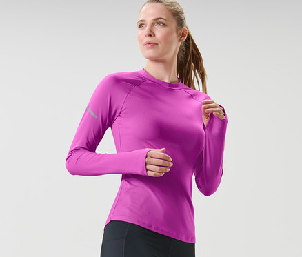 Žena v černých legínách a neonově bobulovém funkčním triku s dlouhým rukávem běží.