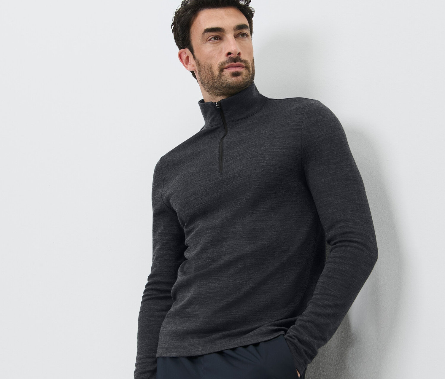 Muž pózuje na bílém pozadí a má na sobě funkční triko s vlnou s certifikací RWS a tmavé kalhoty.