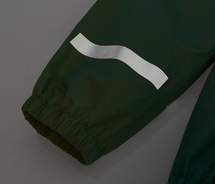 Detail dětských kalhot do deště trávově zelené barvy s reflexním pruhem.