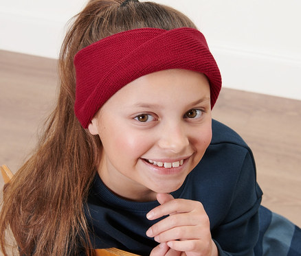 Dívka sedí na židli a má na sobě dětskou pletenou čelenku.