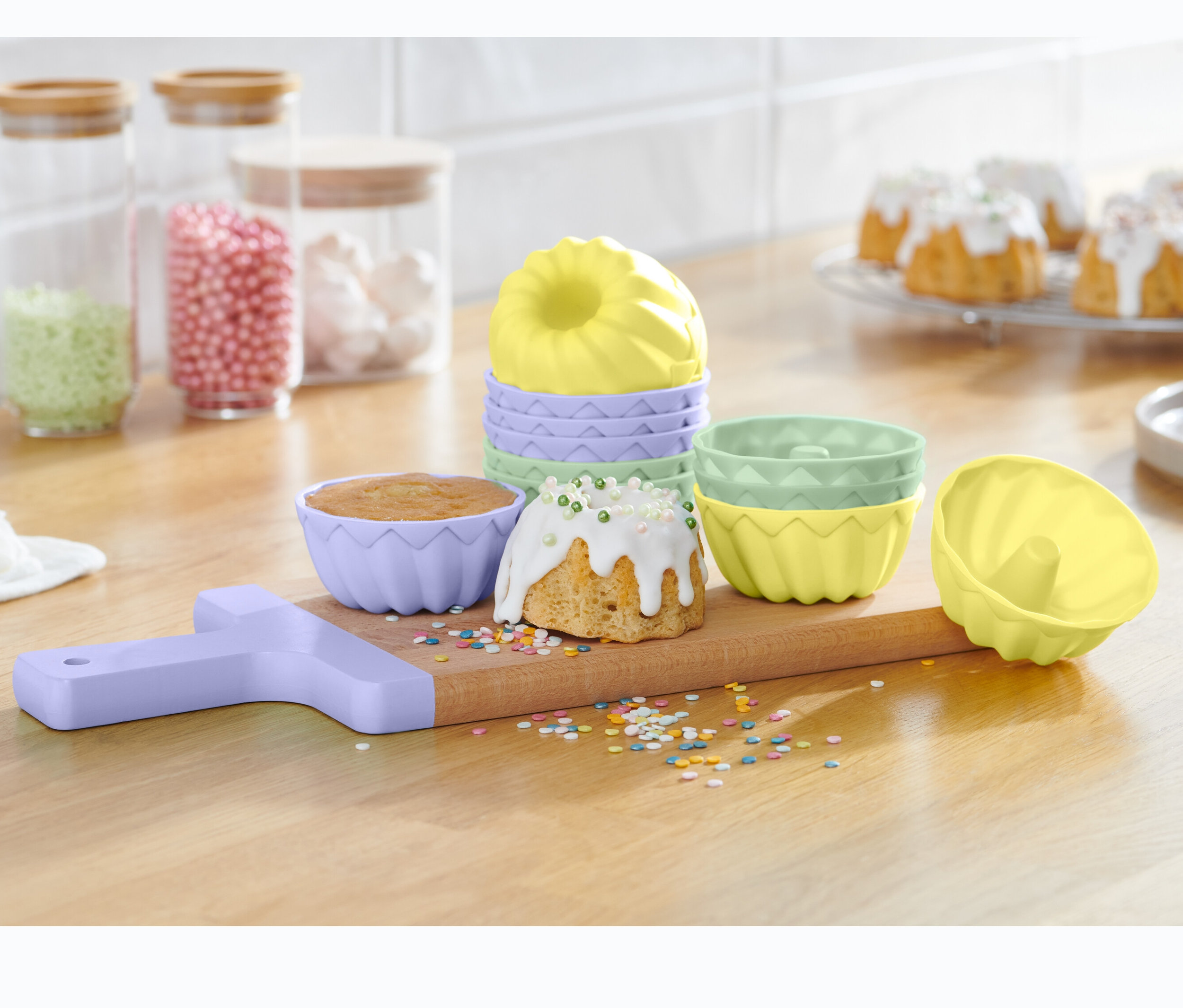 Na dřevěném prkénku jsou formičky na mini bábovky, 12 ks, spolu s upečenými bábovkami a posypem.