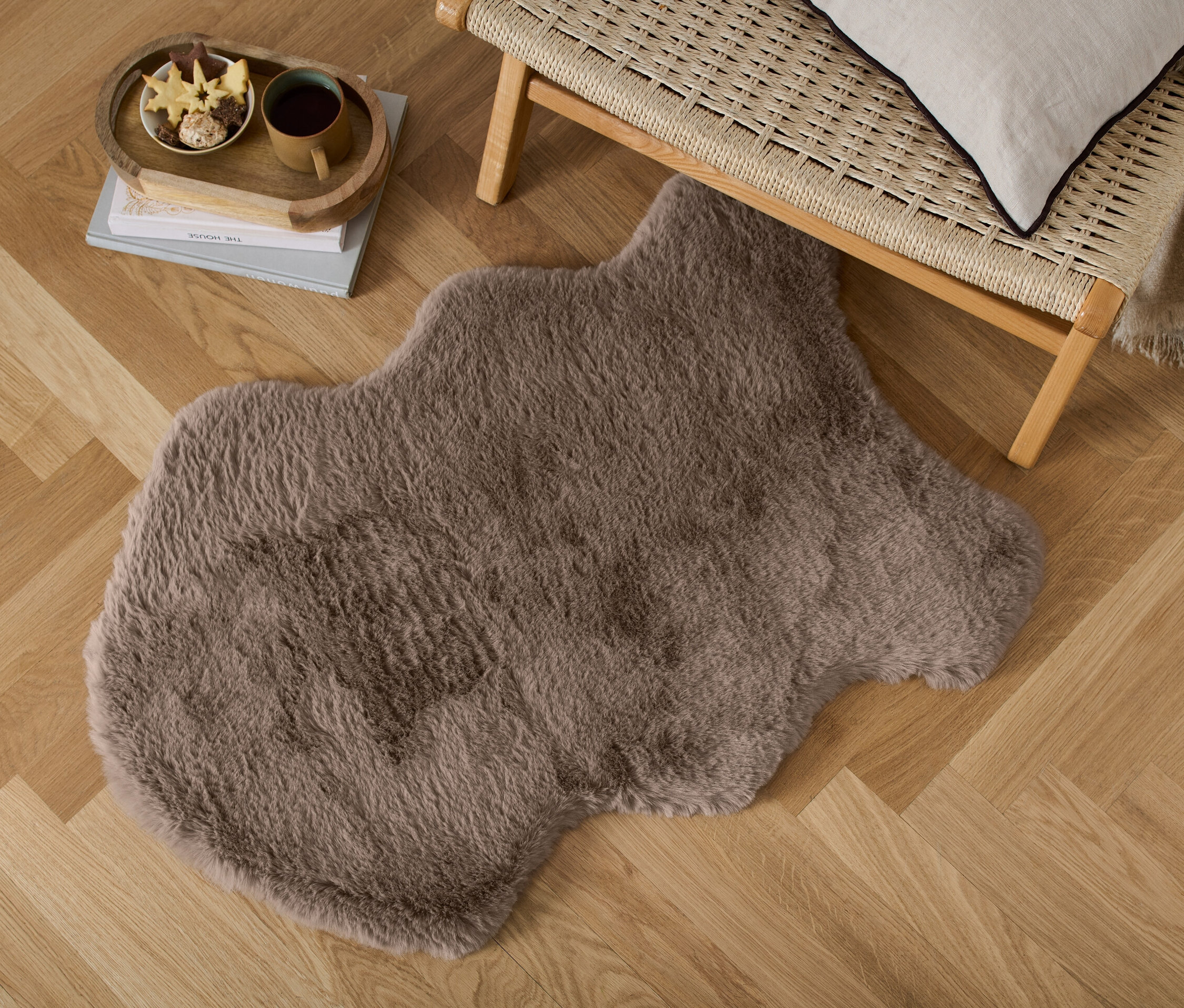 Dekorativní umělá kožešina leží na dřevěné podlaze vedle proutěné lavice.