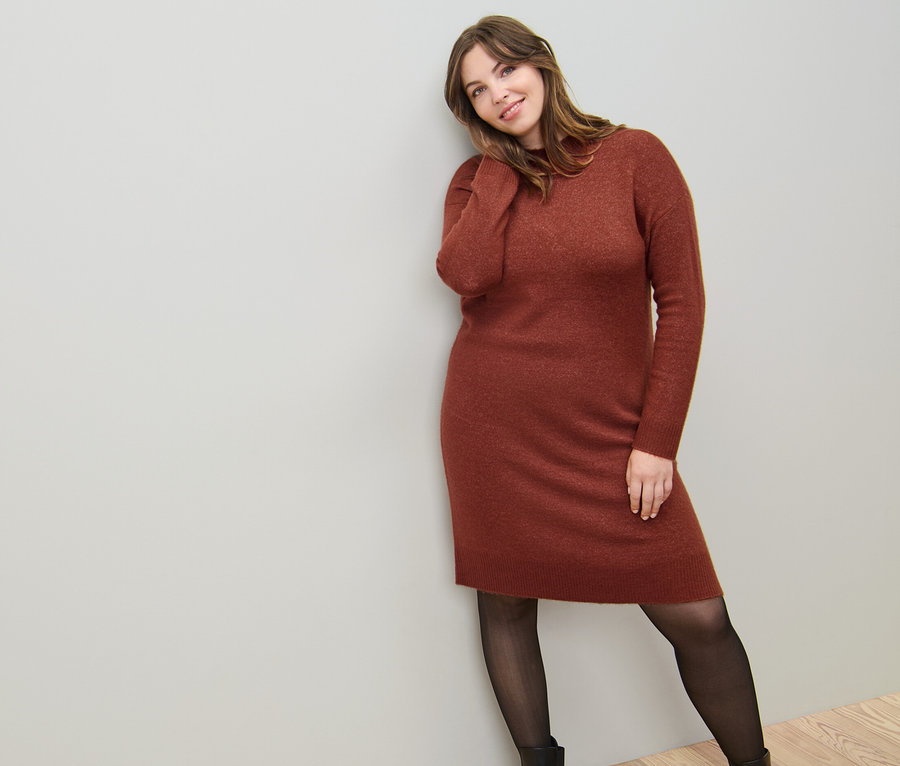 Žena opřená o zeď má na sobě pletené šaty s vlnou a jemné průhledné punčocháče 50 DEN.