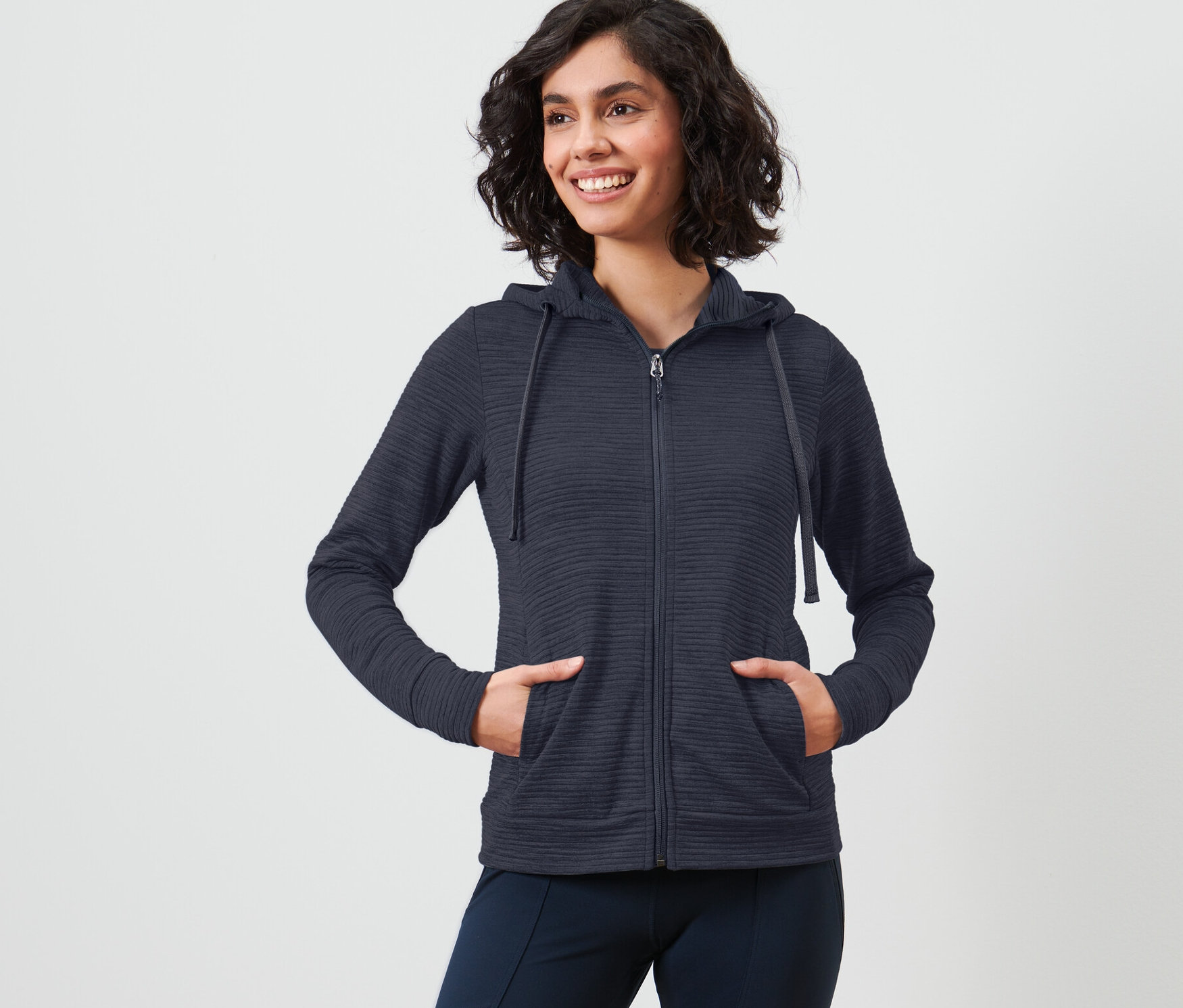 Žena s krátkými vlasy pózuje v modré bundě s kapucí.