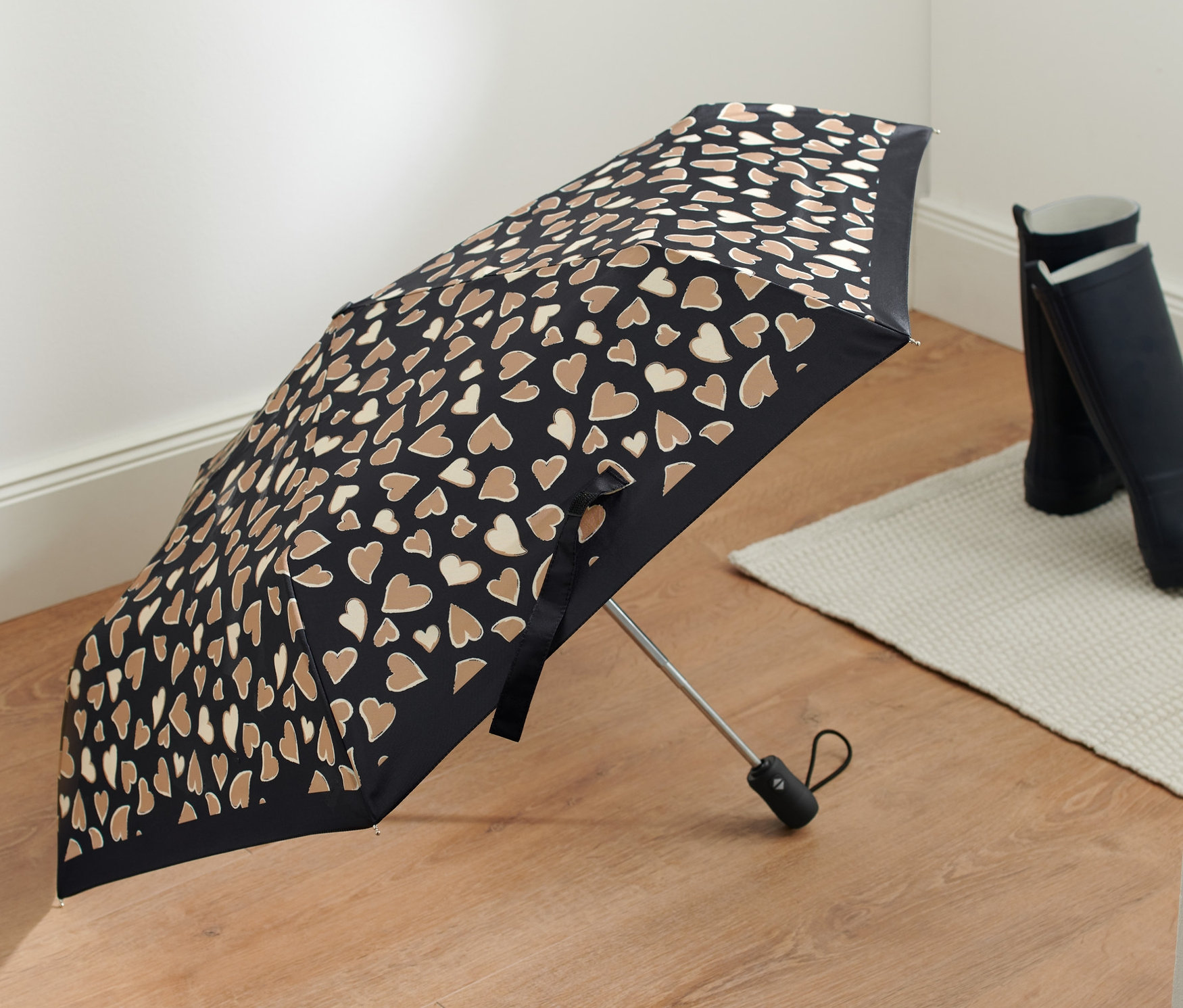 Černý automatický skládací deštník s hnědými srdíčky na podlaze.