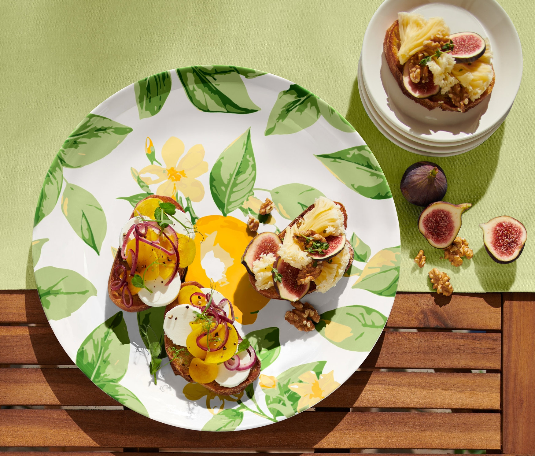 Na servírovacím talíři jsou tři toasty s fíky a sýrem. Na stole jsou i další fíky a ořechy.