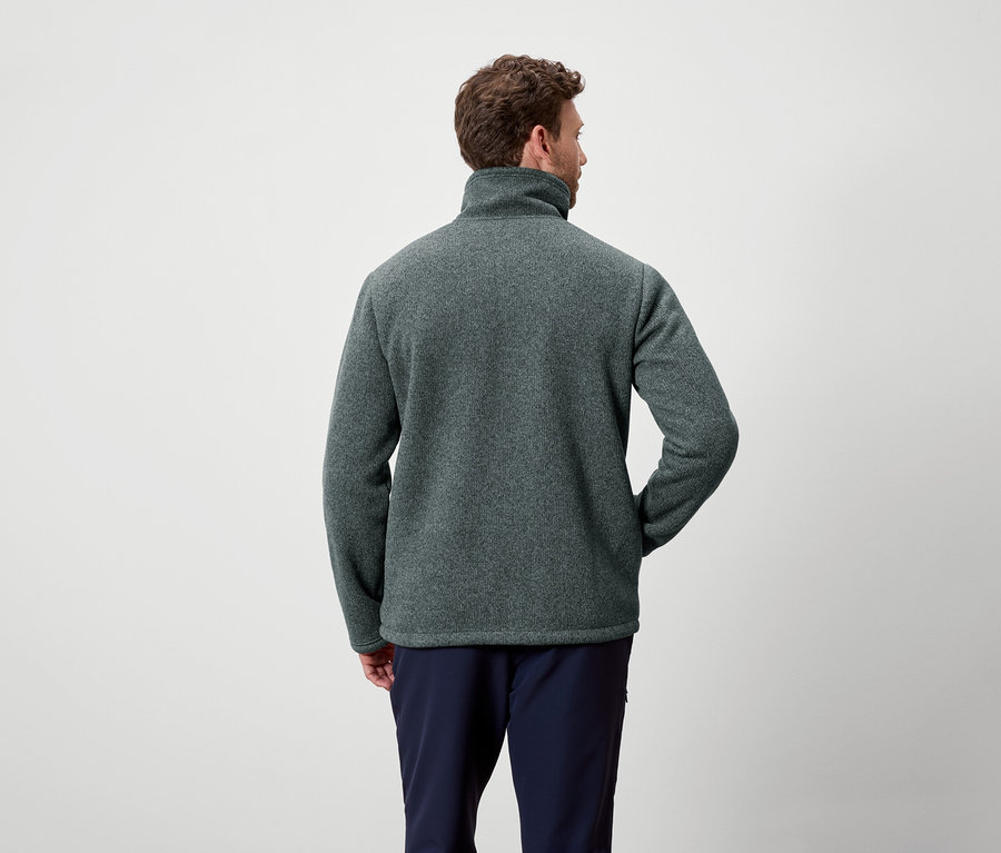 Muž zády ke kameře má na sobě šedozelený fleece a tmavě modré kalhoty.