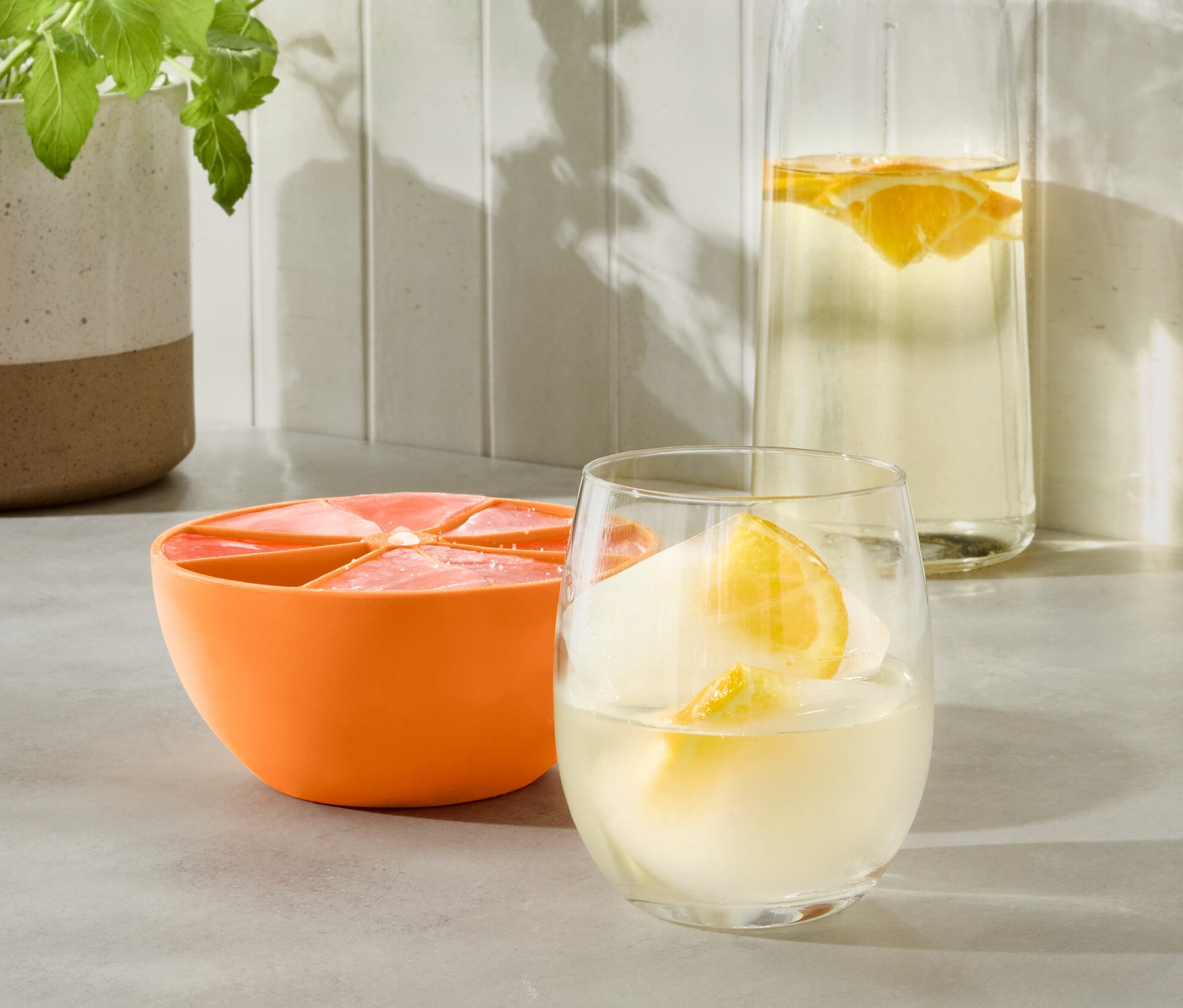 Oranžová forma na led XL vedle sklenice s nápojem a láhve s vodou.