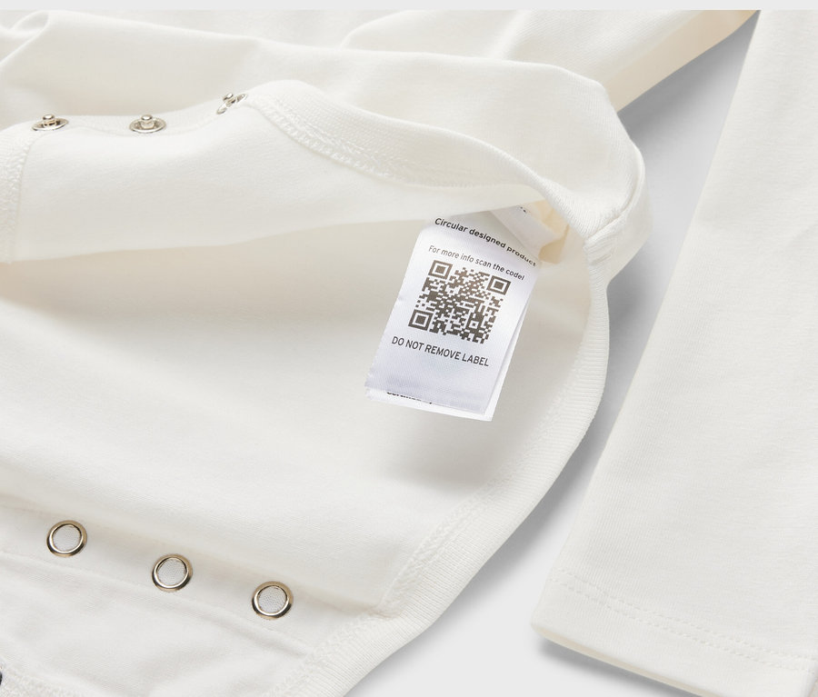 Detail bílého rostoucího body pro miminka s dlouhým rukávem, na kterém je štítek s QR kódem.