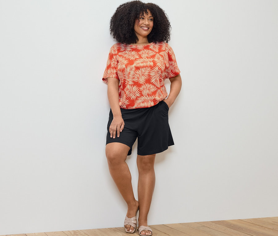 Žena pózuje v halénkovém triku s potiskem a černých žerzejových šortkách.