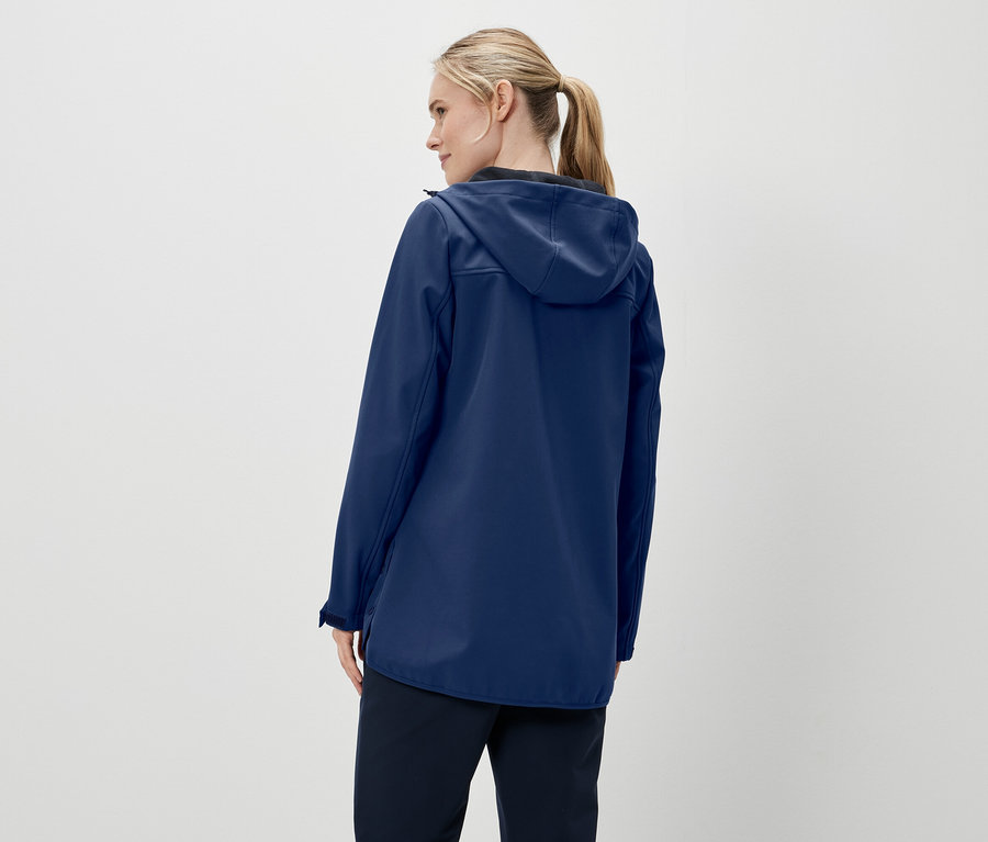 Pohled zezadu na ženu s blond vlasy staženými do culíku, má na sobě tmavě modrou bundu s kapucí a tmavé kalhoty.