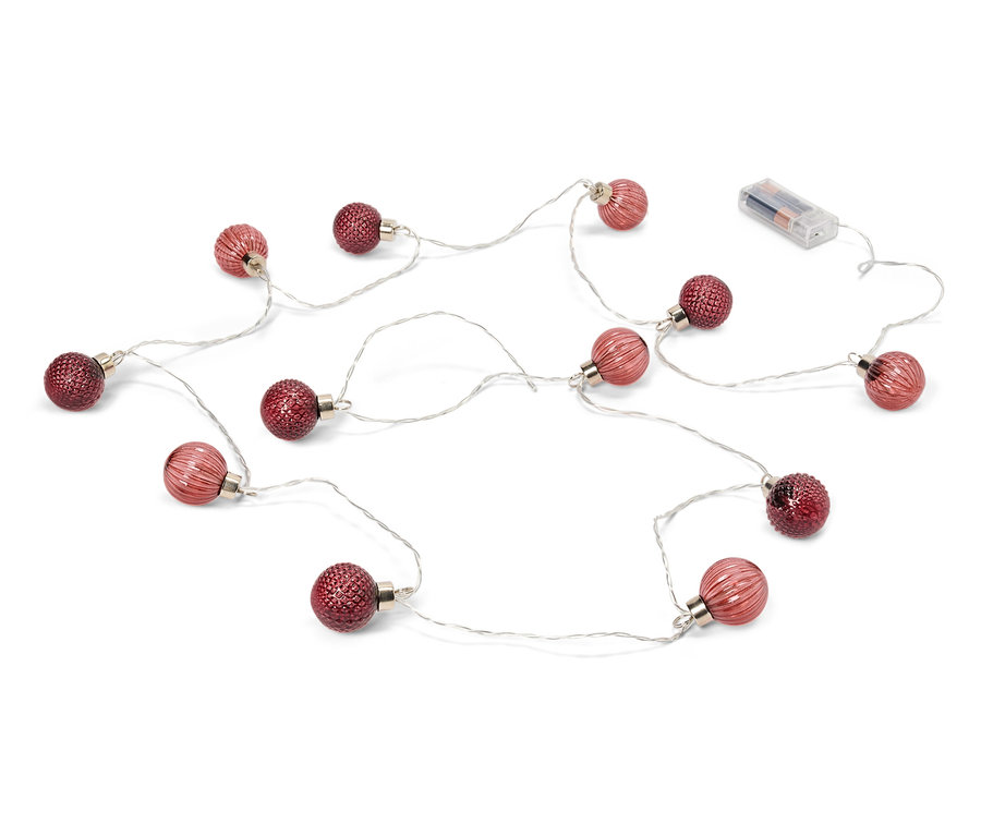 Řetěz světel s červenými baňkami a bateriemi leží na bílém pozadí.