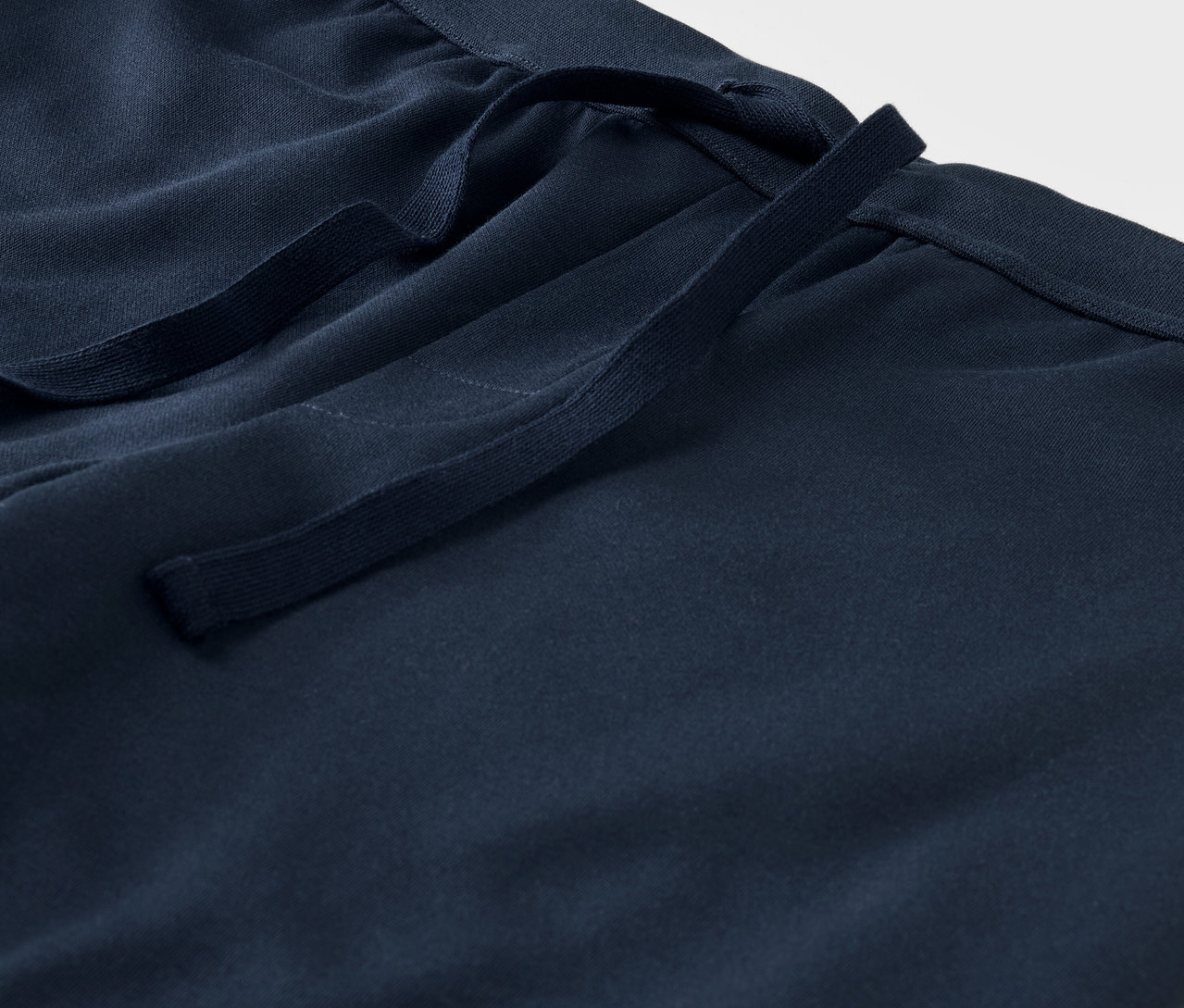 Detail modrých látkových kalhot se stahovací šňůrkou v pase.