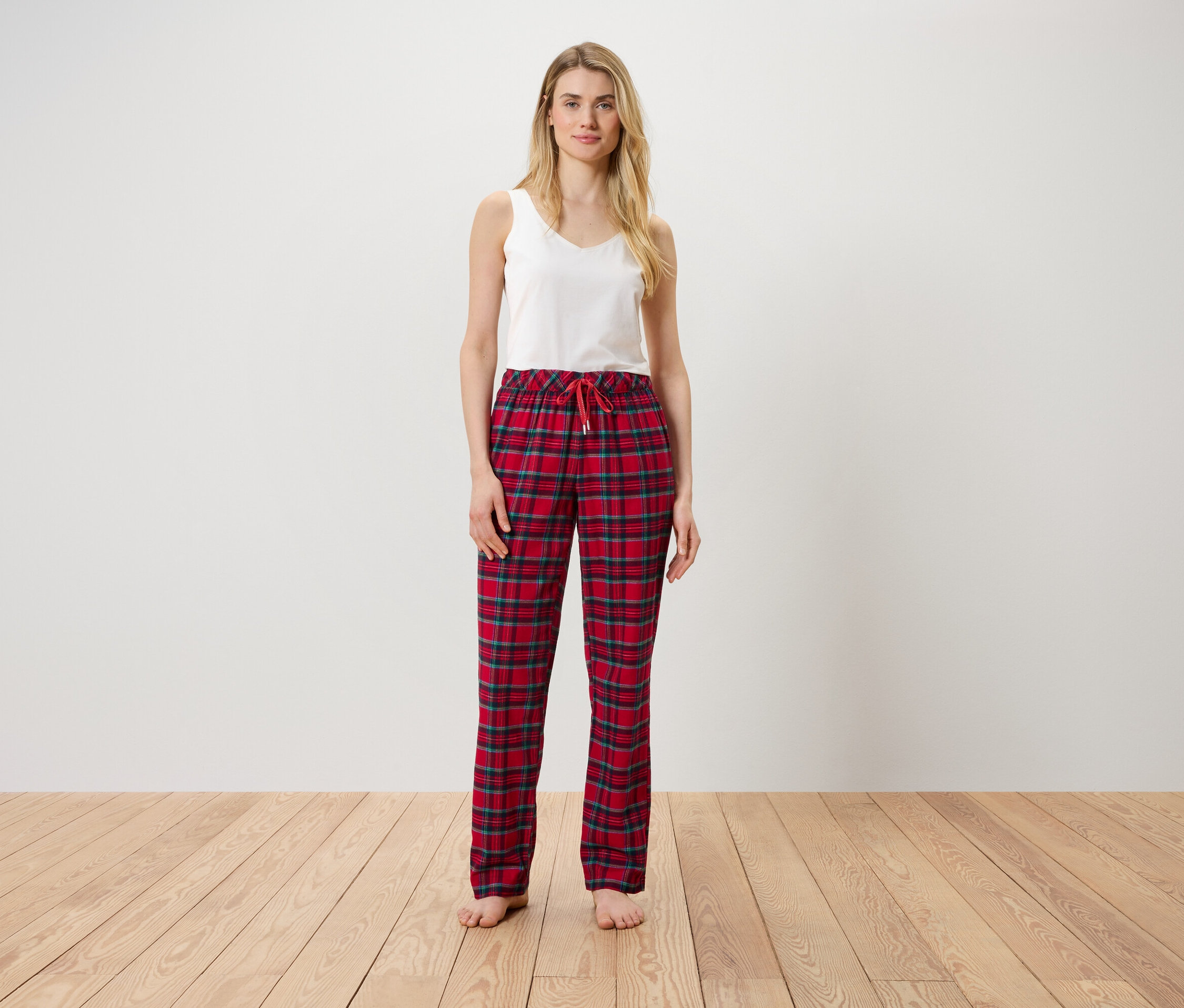 Žena stojí a má na sobě bílý top a červené kostkované kalhoty.