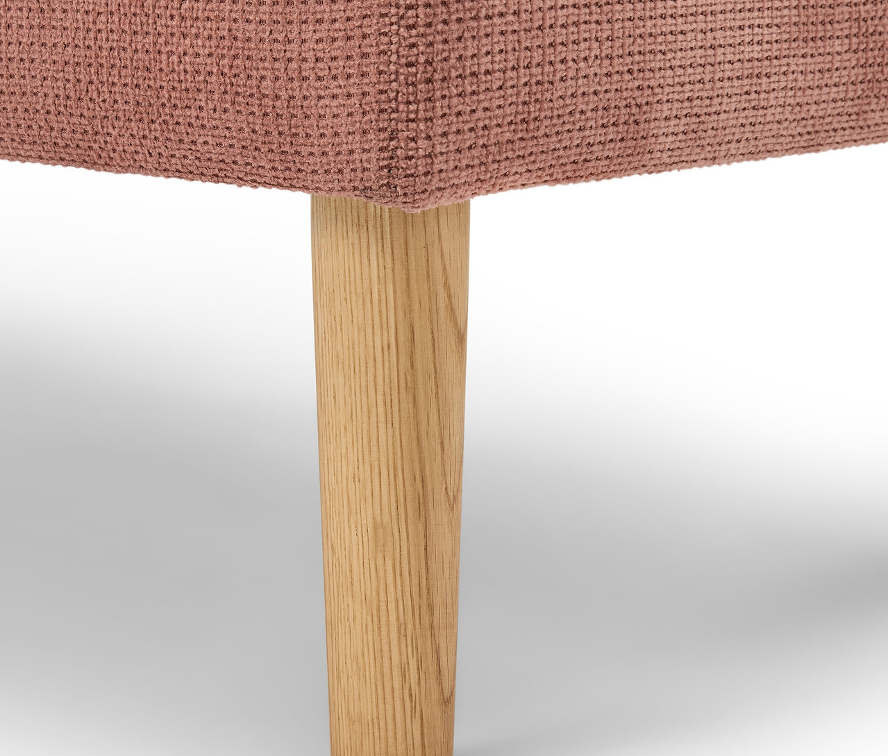 Detail růžového čalouněného nábytku s dřevěnou nohou.