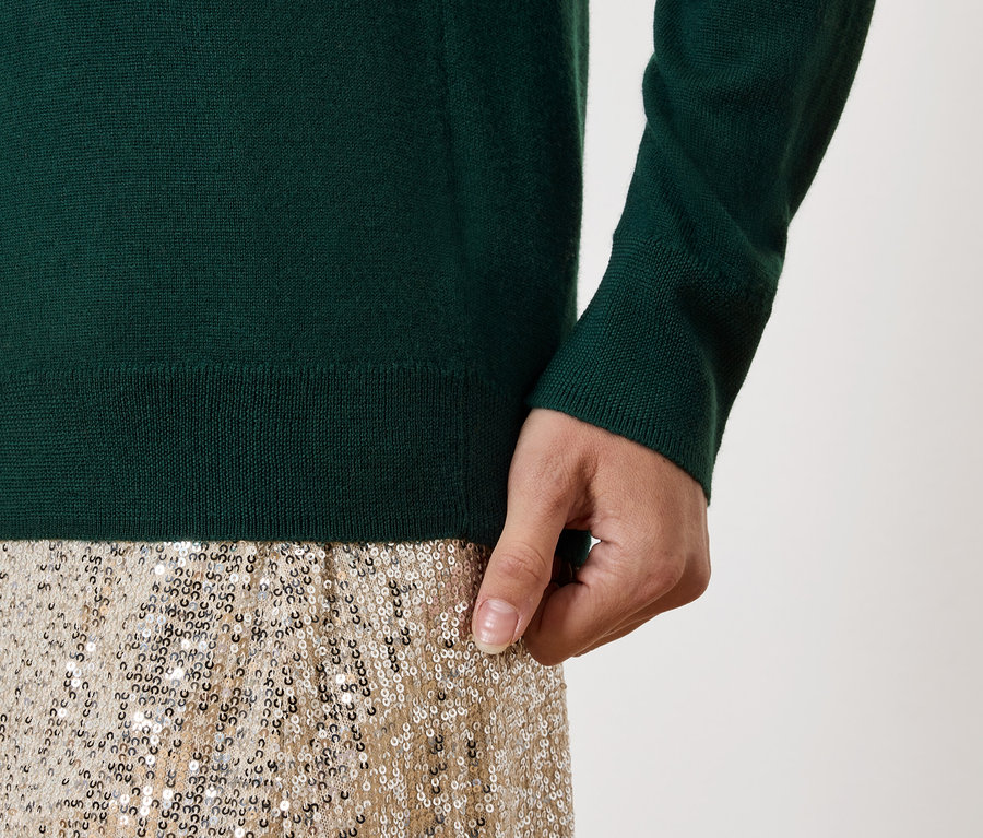 Detail dámského outfitu: zelený svetr a zlatá sukýnka s flitry.