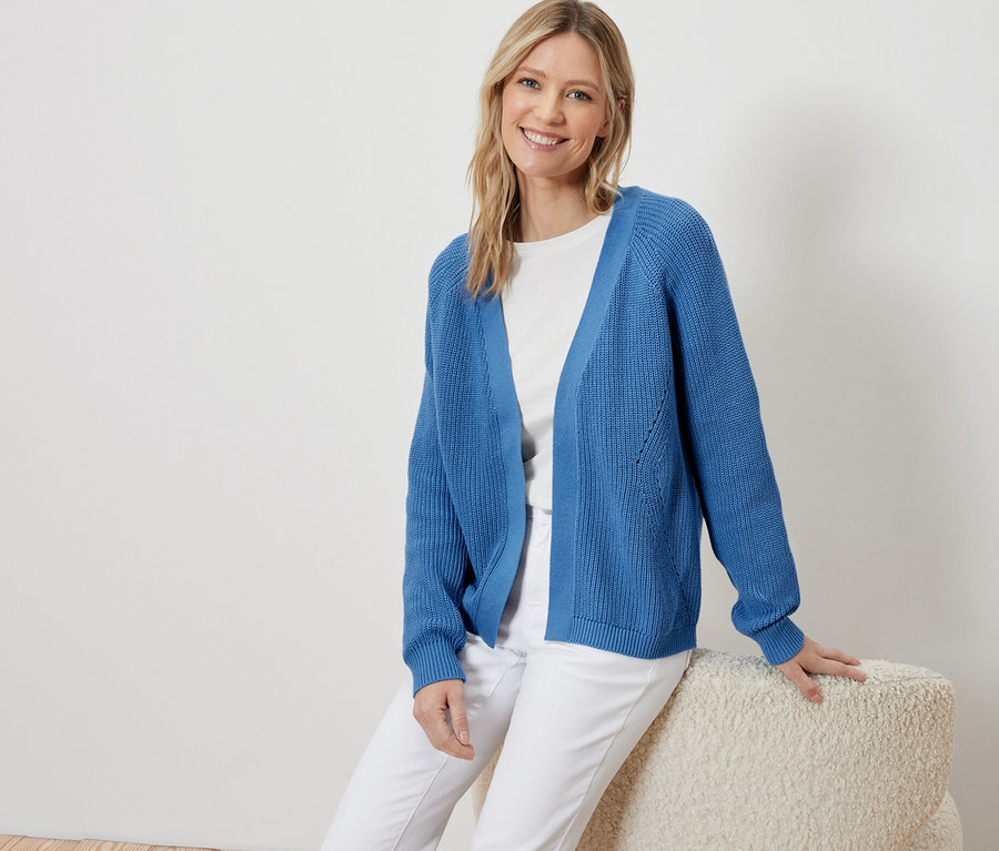 Žena sedí a má na sobě modrý otevřený kardigan.