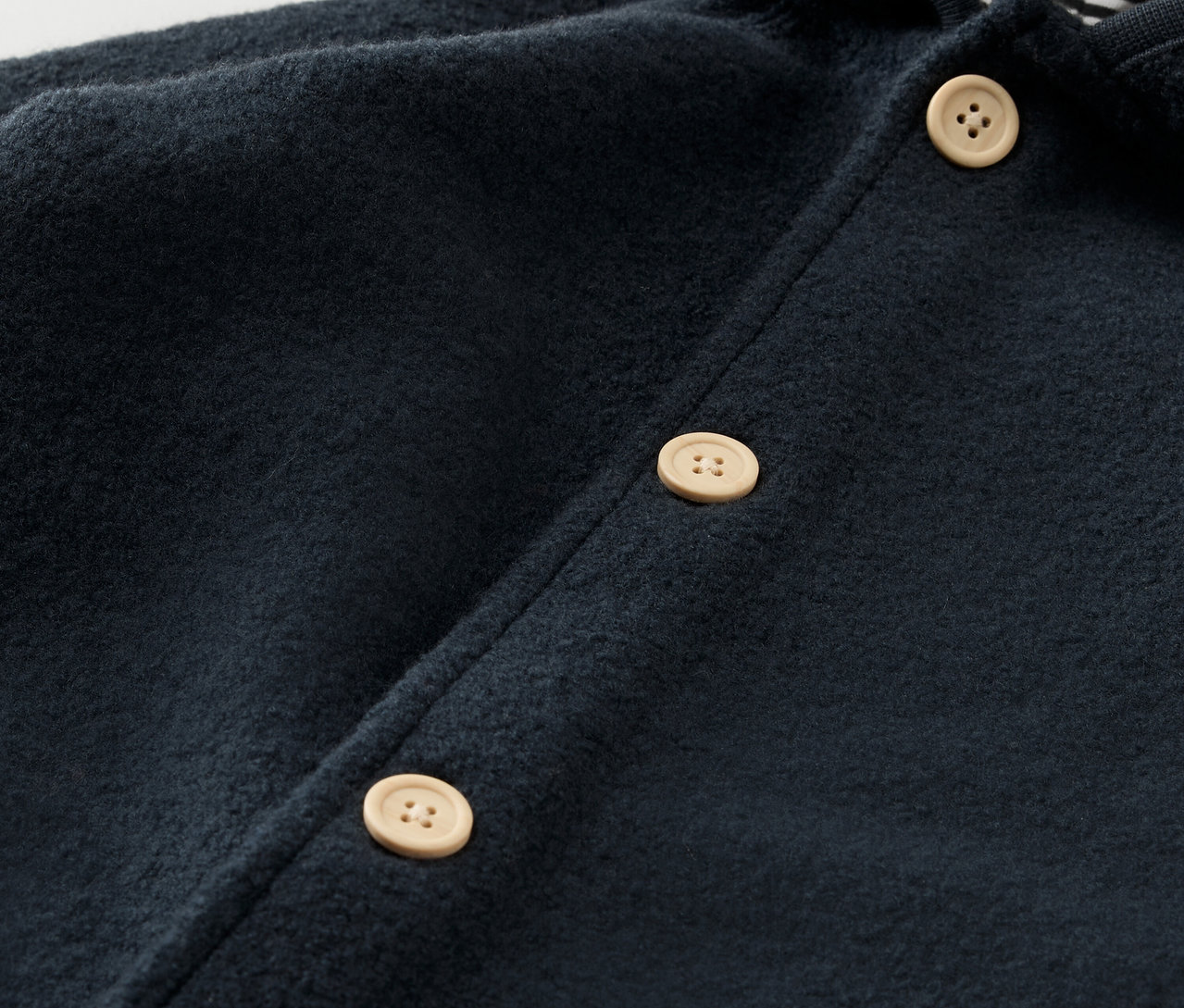 Detail modrého dětského overalu s vlnou merino a světlými knoflíky.