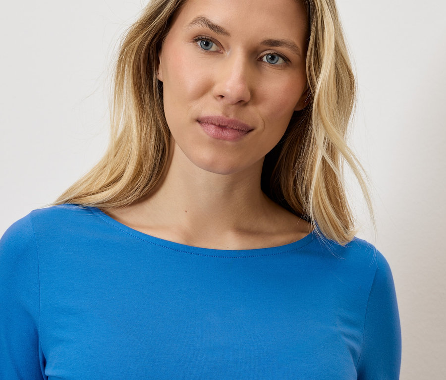 Portrét blondýny v modrém topu s dlouhým rukávem.