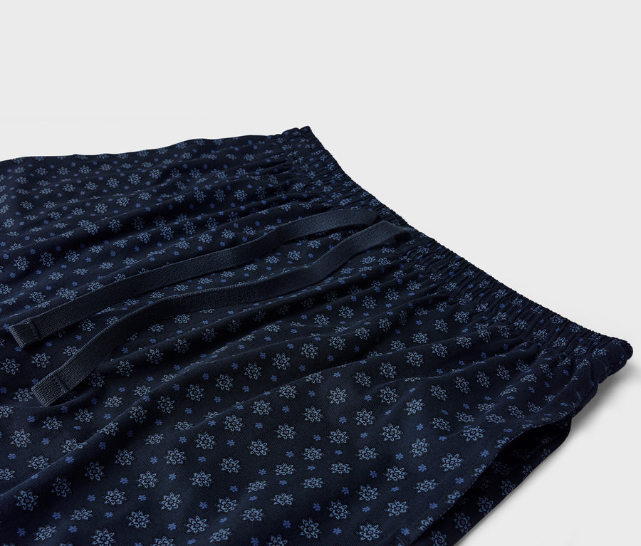 Detailní záběr na tmavě modré pyžamové kalhoty s modrým květinovým vzorem a stahovací šňůrkou.