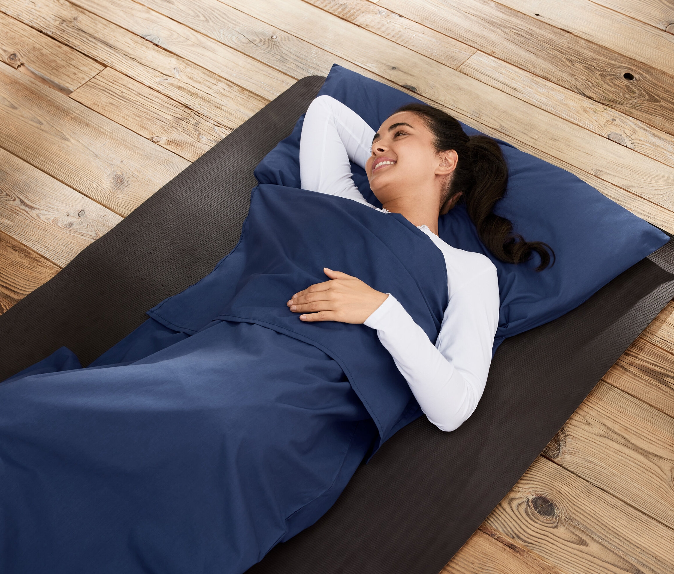 Žena leží ve vložce do spacího pytle na podložce na dřevěné podlaze.