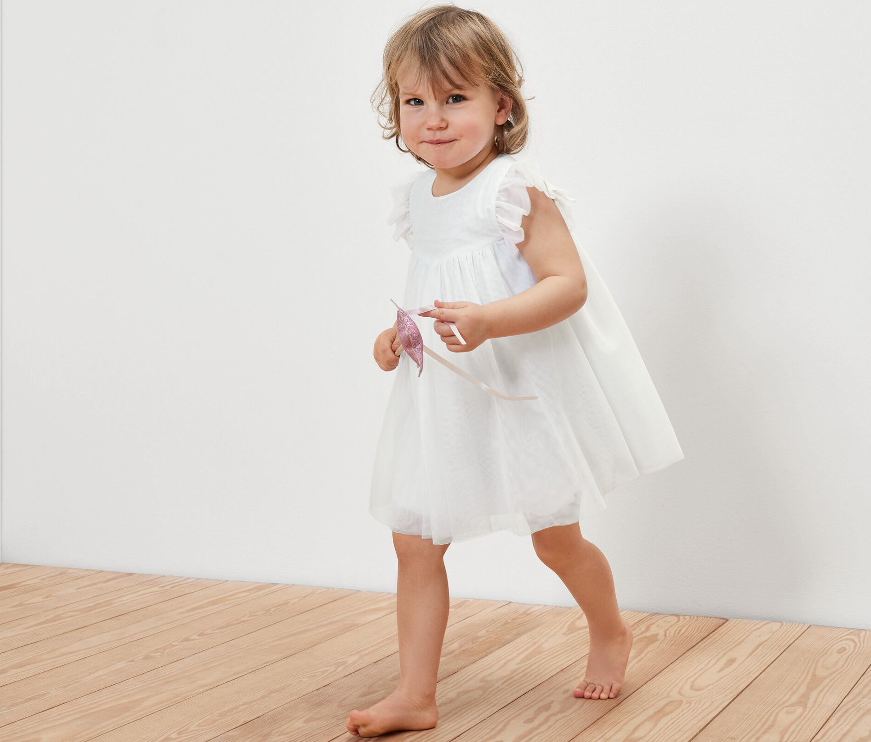 Holčička v tylových šatech kráčí po dřevěné podlaze.