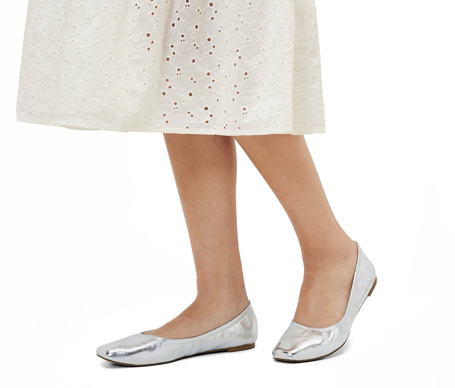 Nohy ženy v bílých šatech a kožených balerínách.