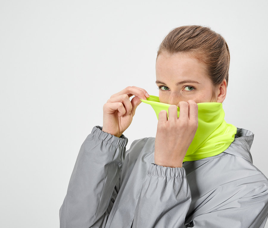 Žena si přetahuje přes obličej neonově žlutý nákrčník a má na sobě šedou bundu.