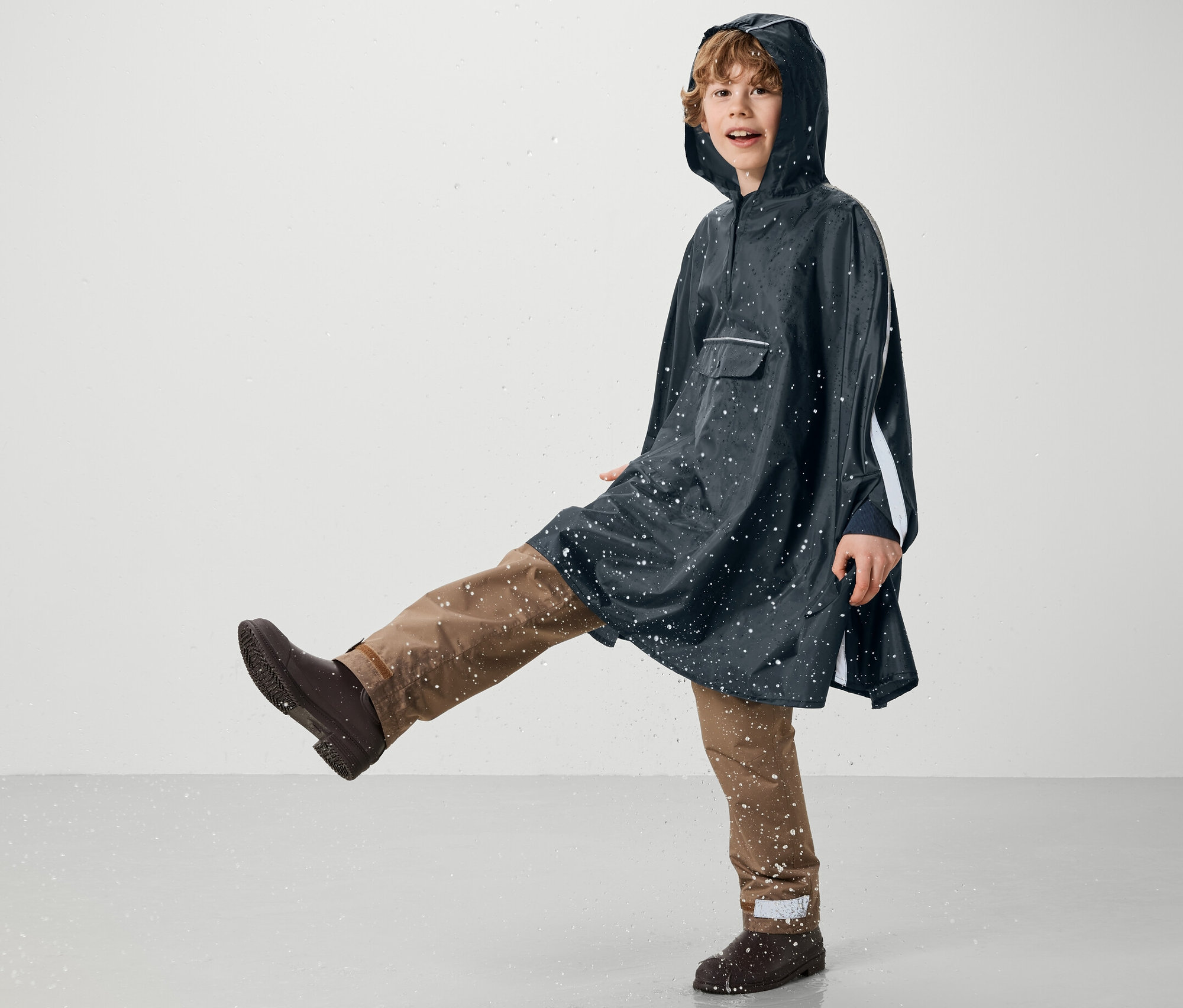 Chlapec v modrém dešťovém ponču Kinder-Regenponcho kope do vody.