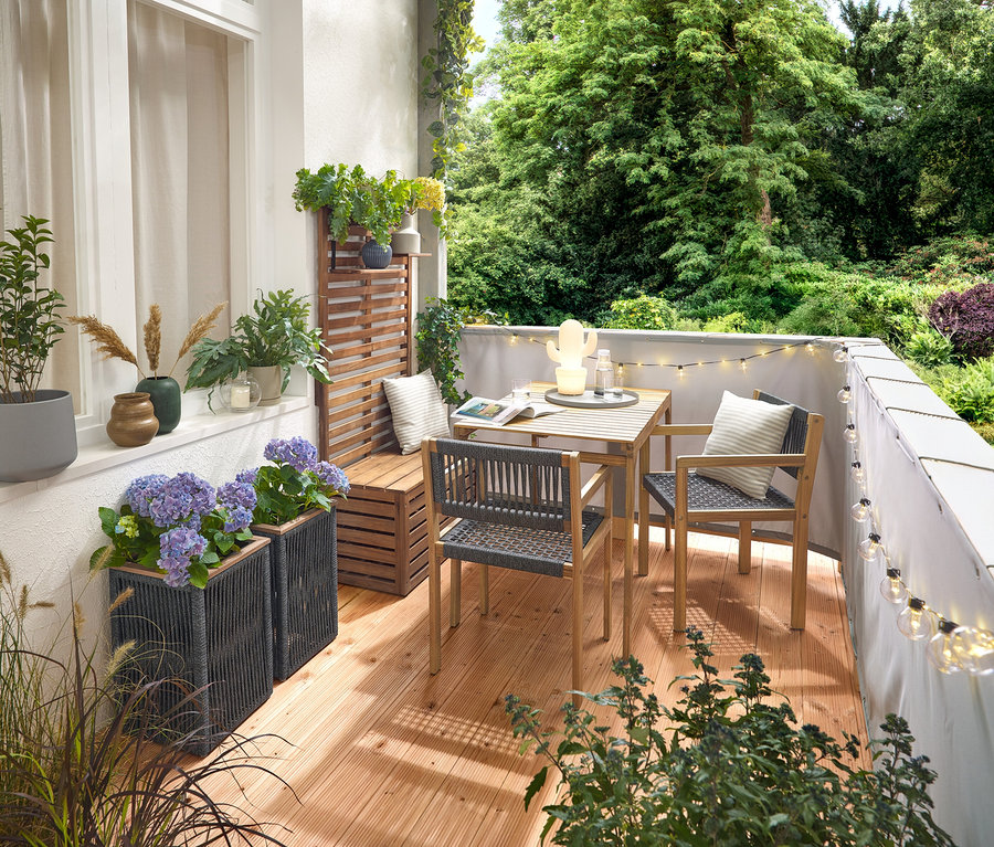 Zařízení balkonu s balkónovou soupravou s textilní výplní, šedou balkónovou zástěnou a ochranou proti větru, venkovním světelným řetězem s LED a síťovým adaptérem, květináčem s textilní výplní, venkovní LED dobíjecí stolní lampou, kaktus a 2 venkovními polštáři s lněným omakem.