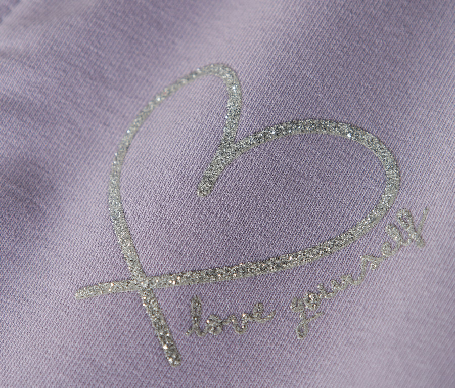 Detail fialového oděvu s třpytivým srdíčkovým vzorem a textem "love yourself".