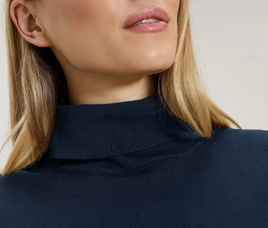 Detailní záběr ženy s blond vlasy v tmavě modrém roláku.