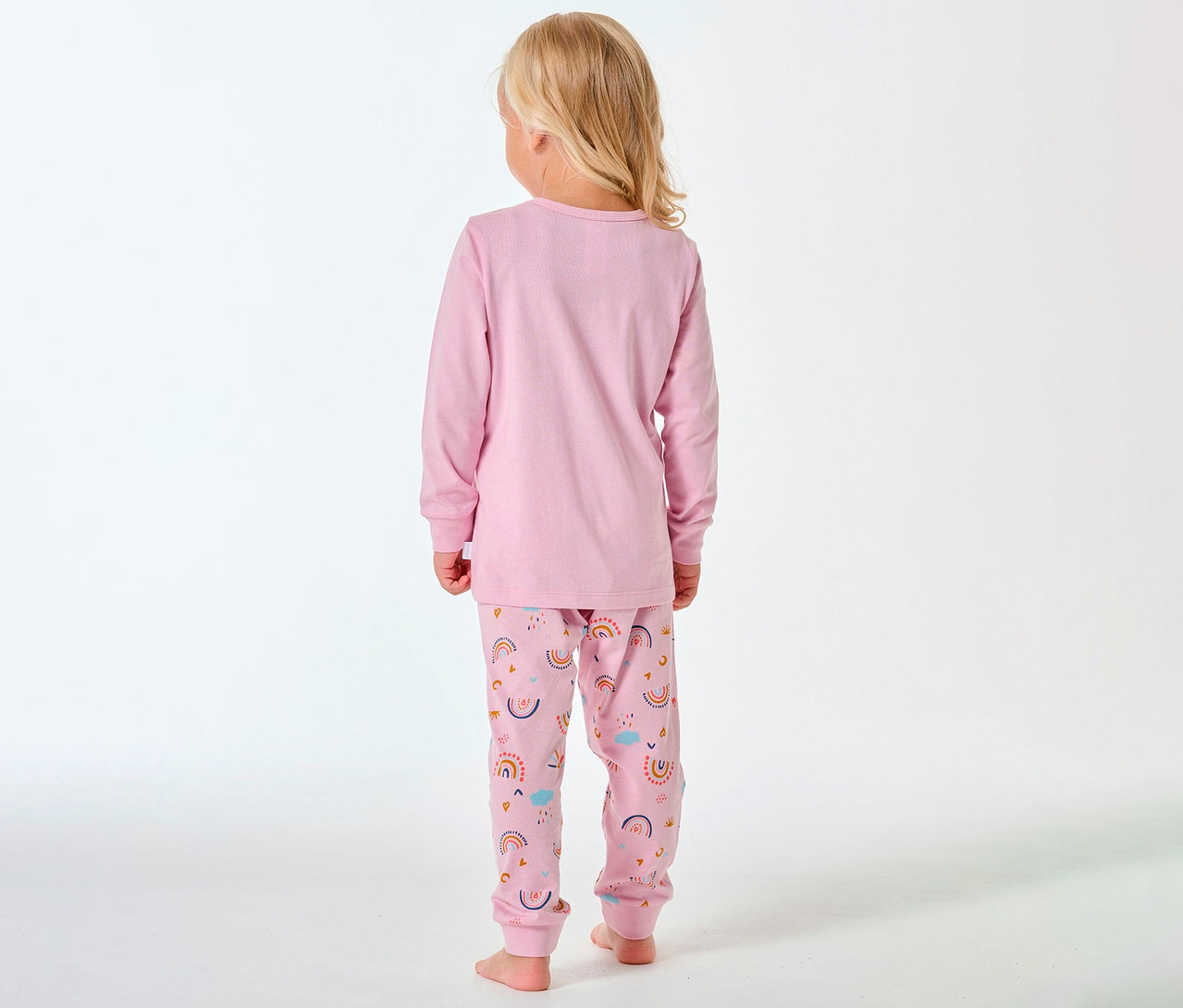 Dítě zezadu s blond vlasy má na sobě dlouhé dětské pyžamo SCHIESSER s duhovým vzorem.