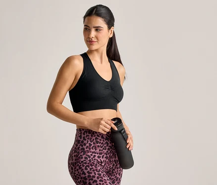 Žena ve sportovní podprsence a legínách s leopardím vzorem drží černou láhev na vodu.