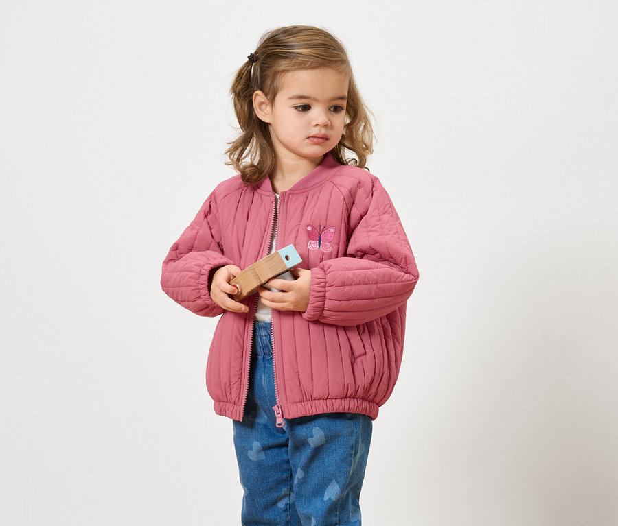 Dívka v růžové bundě drží dřevěnou hračku.