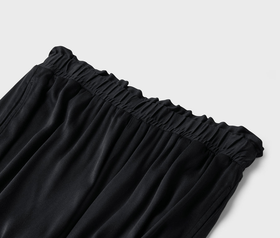 Detailní záběr černých kalhot s elastickým pasem.