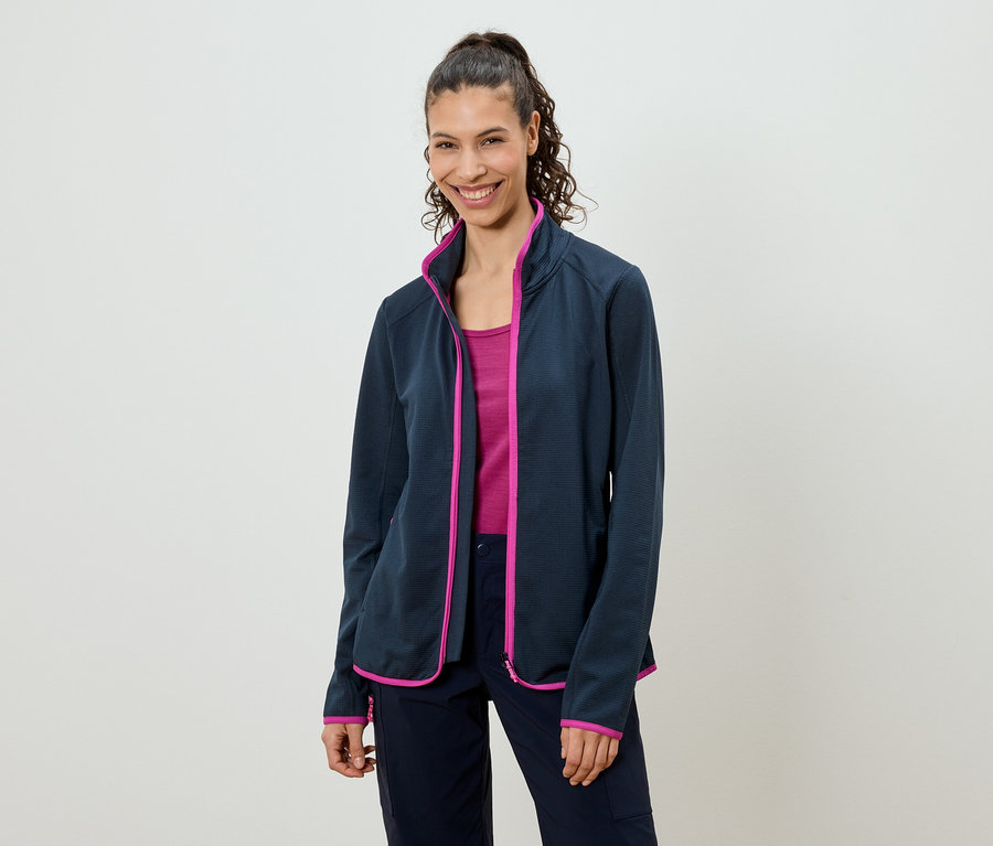 Žena s culíkem má na sobě tmavě modrou fleecovou bundu s růžovými akcenty, růžový top a tmavě modré kalhoty.