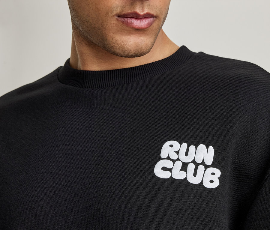 Detail muže v černé mikině s bílým nápisem 'RUN CLUB'.
