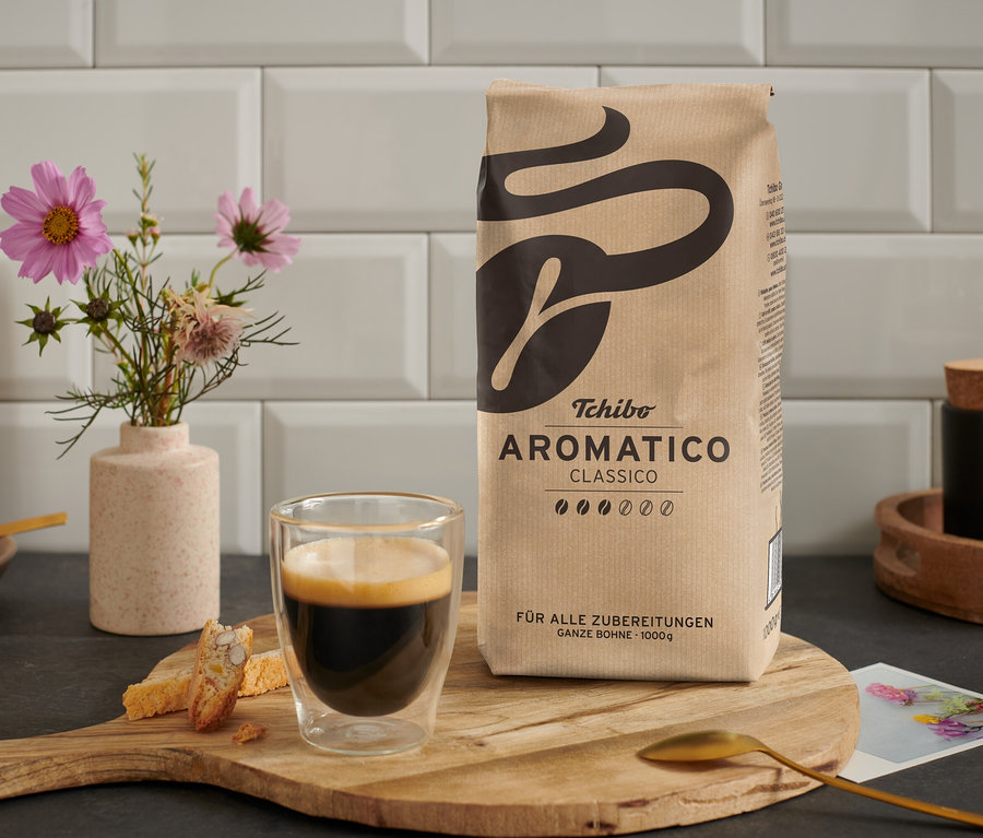 Šálek kávy stojí vedle balení Aromatico Classico - 1 kg zrnkové kávy na dřevěném stole.
