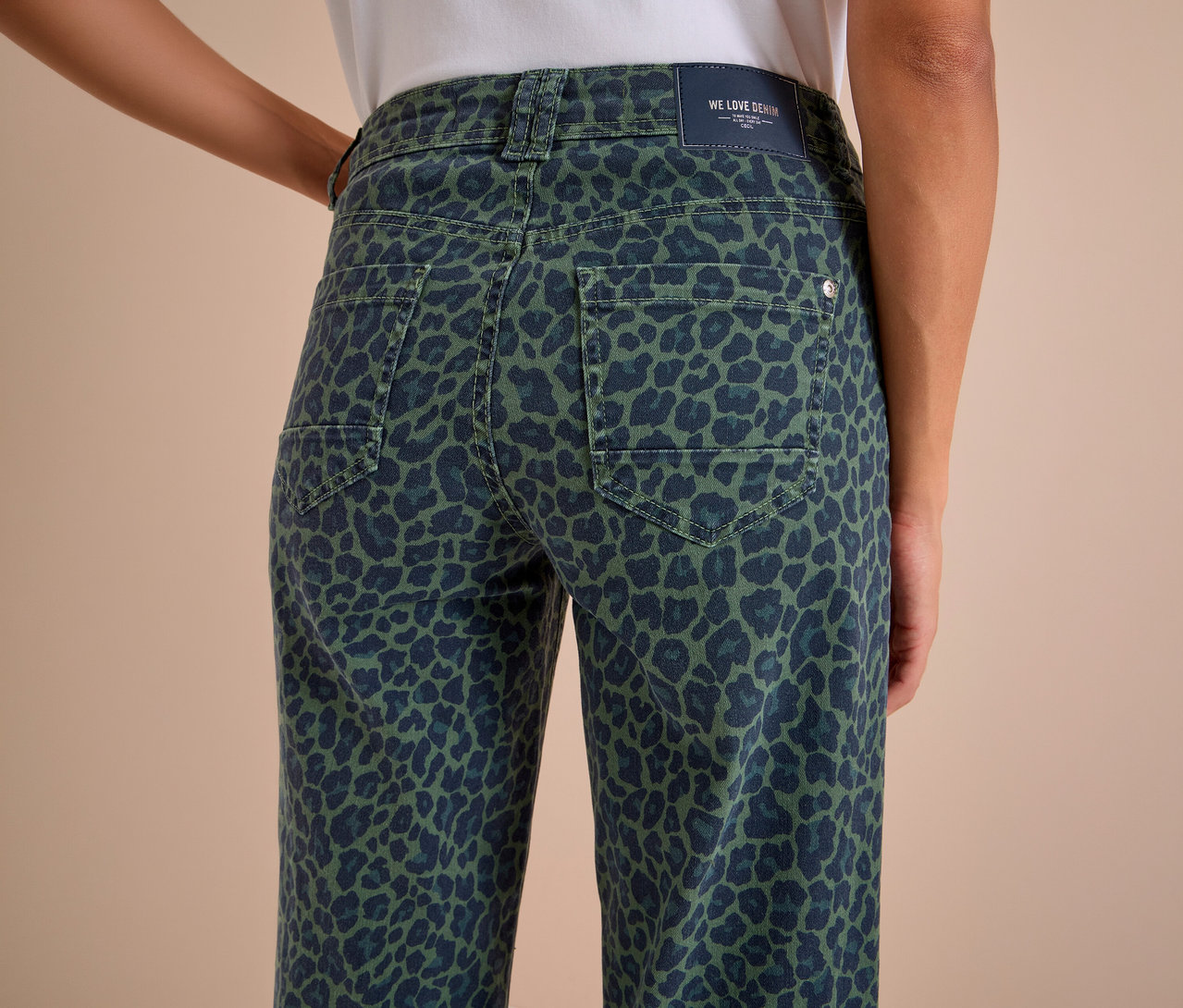 Zadní pohled na osobu v zeleno-tmavě modrých Džínech CECIL s leopardím vzorem, viditelnými zadními kapsami a štítkem „WE LOVE DENIM“.