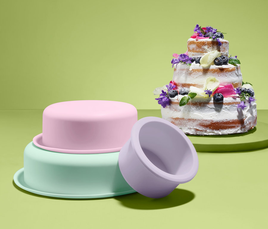 Vícepatrový dort zdobený květy a vedle sady forem na pečení patrových dortů.