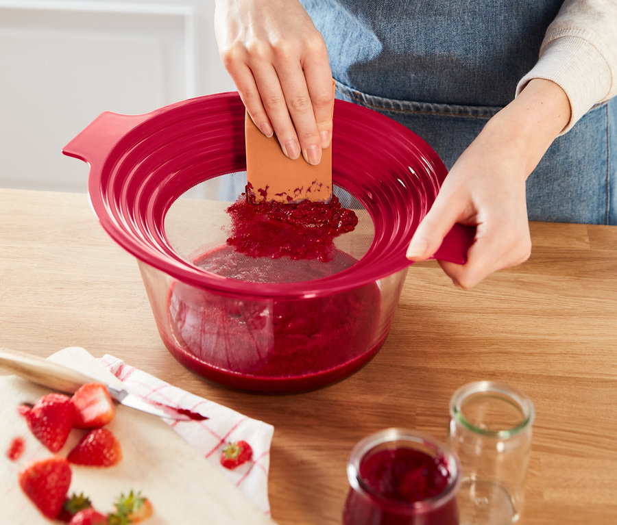 Žena pasíruje jahody přes červené sítko 2 v 1.