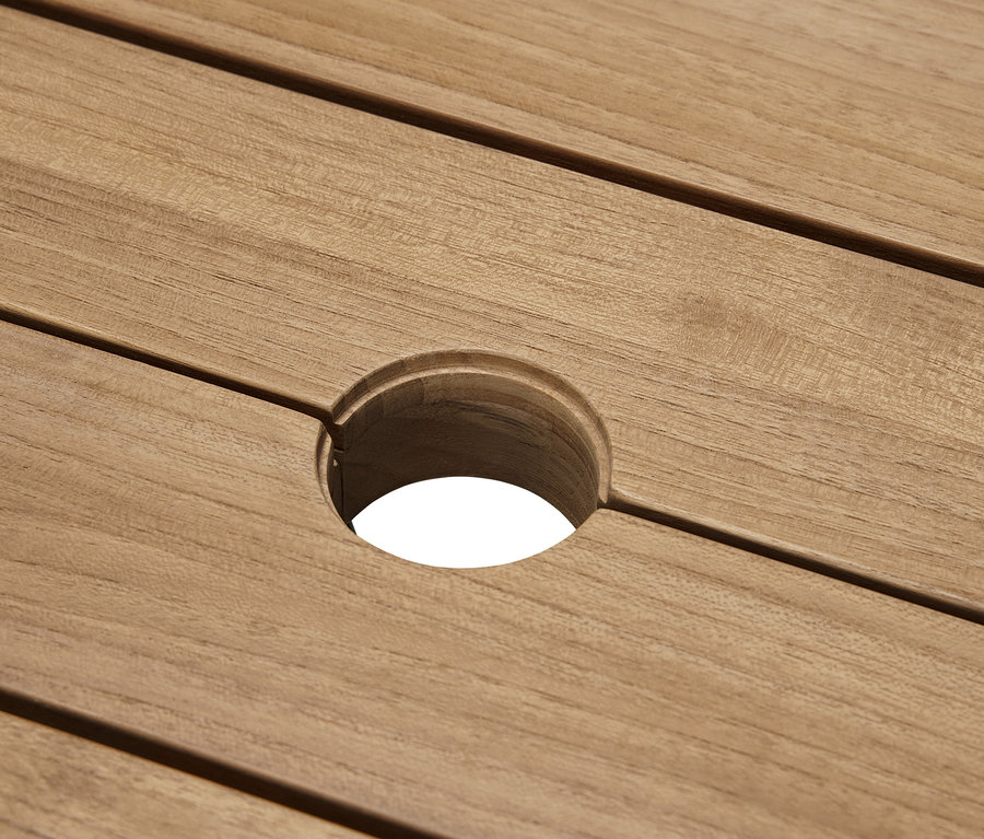 Detail teakového jídelního stolu s moderní nohou ve tvaru X a otvorem uprostřed.