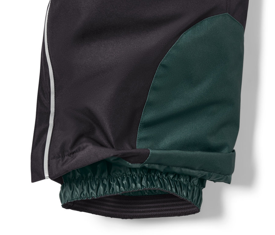 Detail dětských lyžařských kalhot, černé barvy, se zelenou skvrnou na nohavici a elastickým lemem u kotníku.