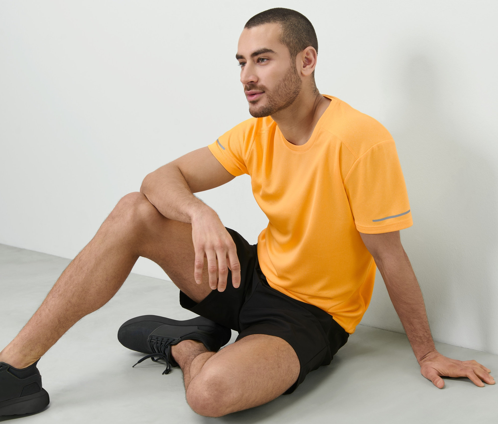 Muž sedí na podlaze a má na sobě broskvové funkční tričko.