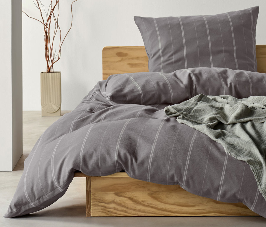 Šedé flanelové povlečení standardní velikosti s hnědošedou dekou na dřevěné posteli.