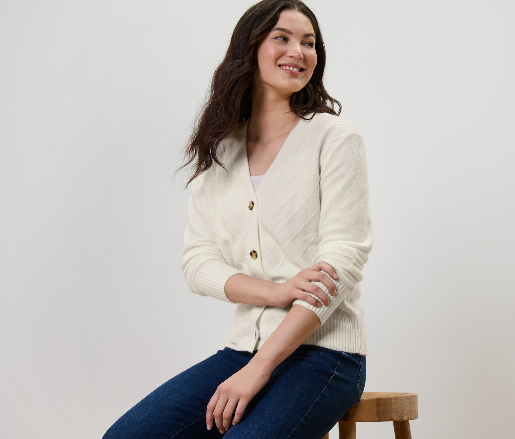 Žena sedí na stoličce a má na sobě krémově bílý kardigan s pletenou strukturou.