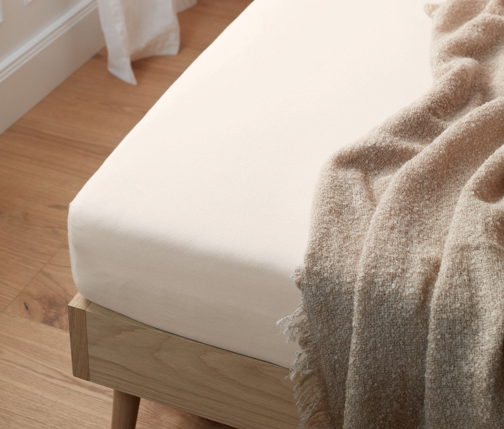 Bílé žerzejové prostěradlo standardní velikosti na posteli s béžovou dekou a dřevěným rámem.