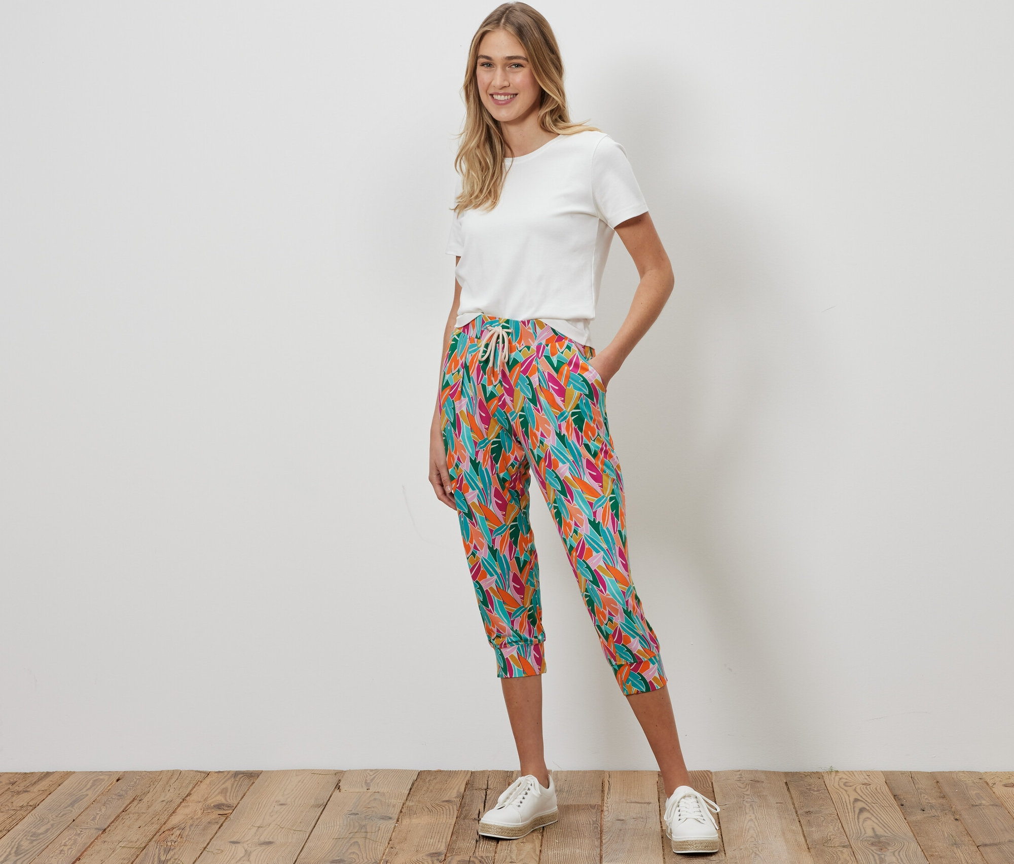 Žena stojí a má na sobě 3/4 žerzejové kalhoty, různé barvy, a bílé tričko.